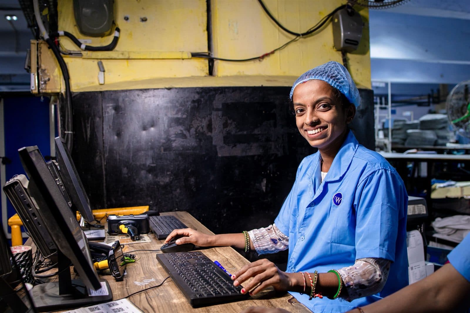 Colaboradora sorri enquanto trabalha em um computador no chão de fábrica.