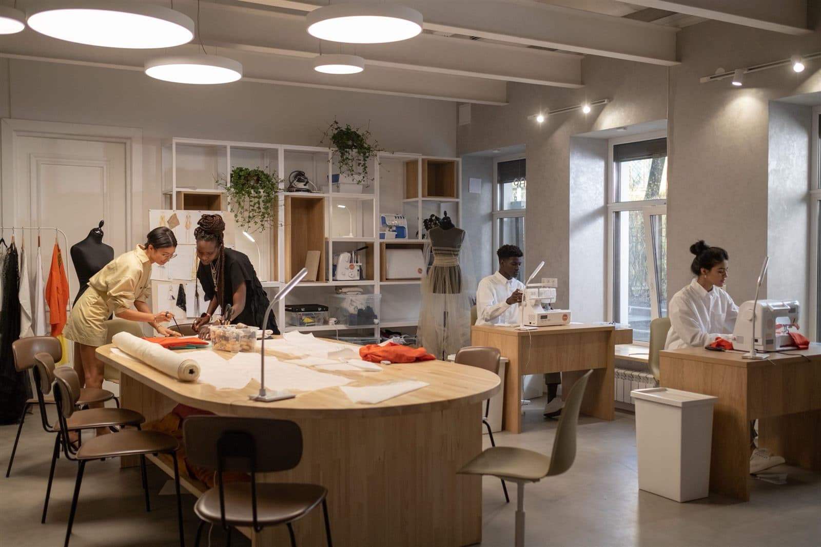 Equipe de um ateliê de moda trabalha em conjunto no desenvolvimento de peças, com fichas técnicas na parede.