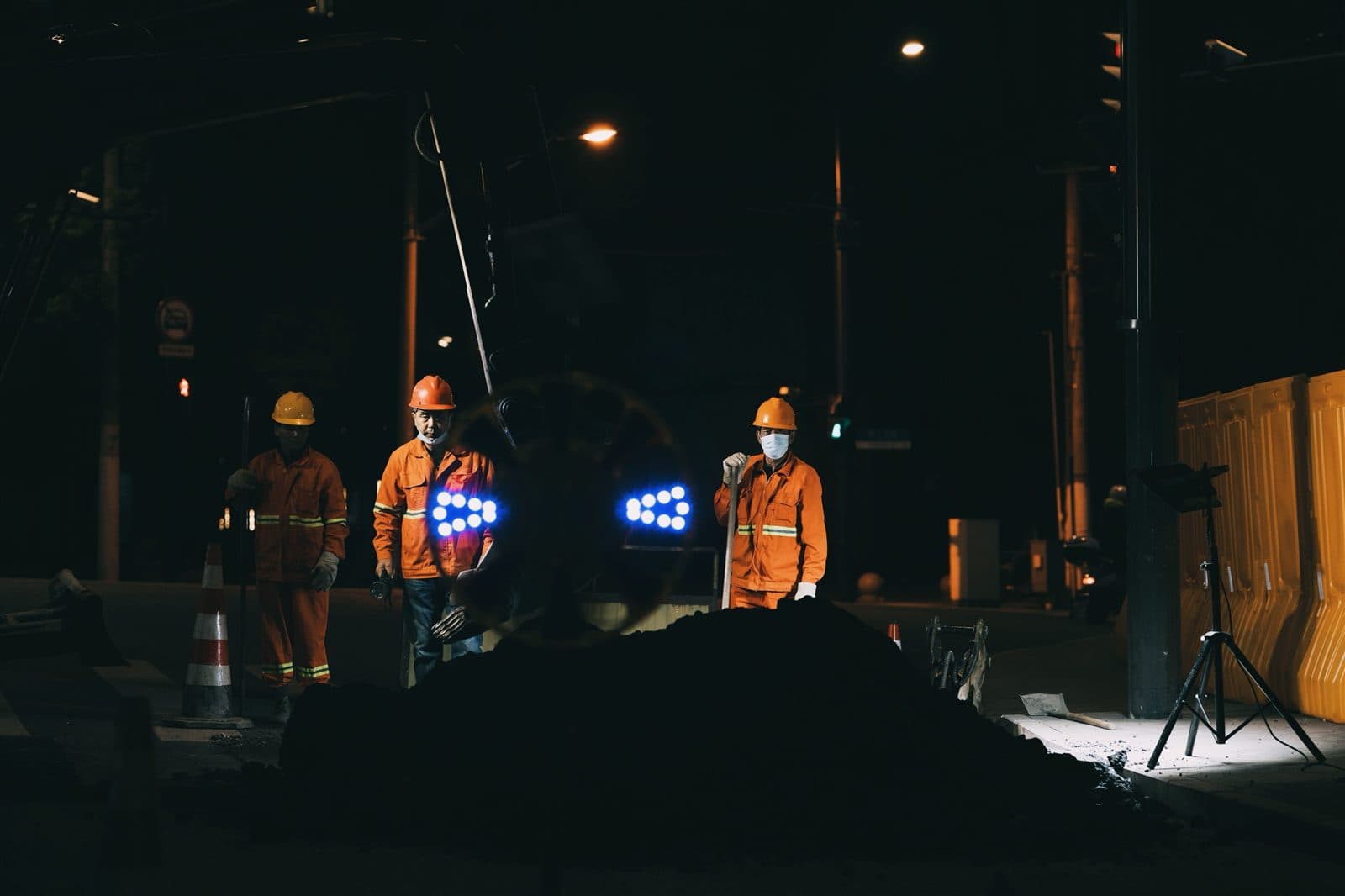 Equipe de operários com capacetes e uniformes de segurança trabalha à noite em uma via pública.