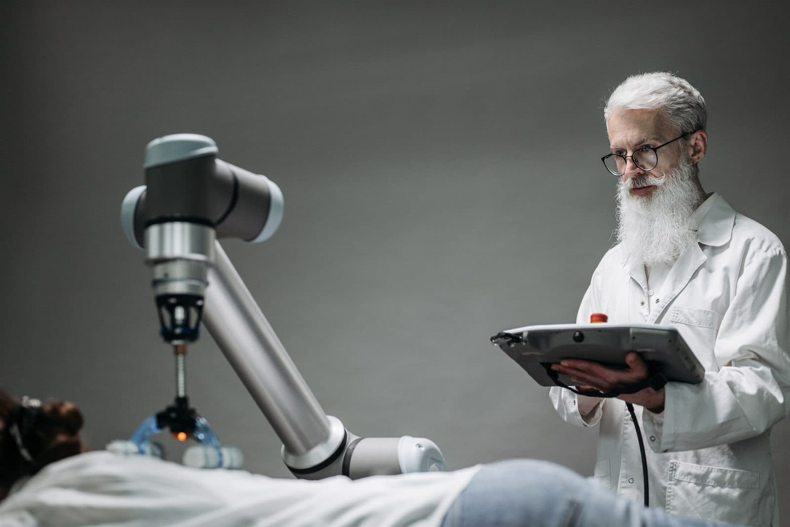 Médico acompanha um procedimento assistido por braço robótico, com um tablet em mãos.